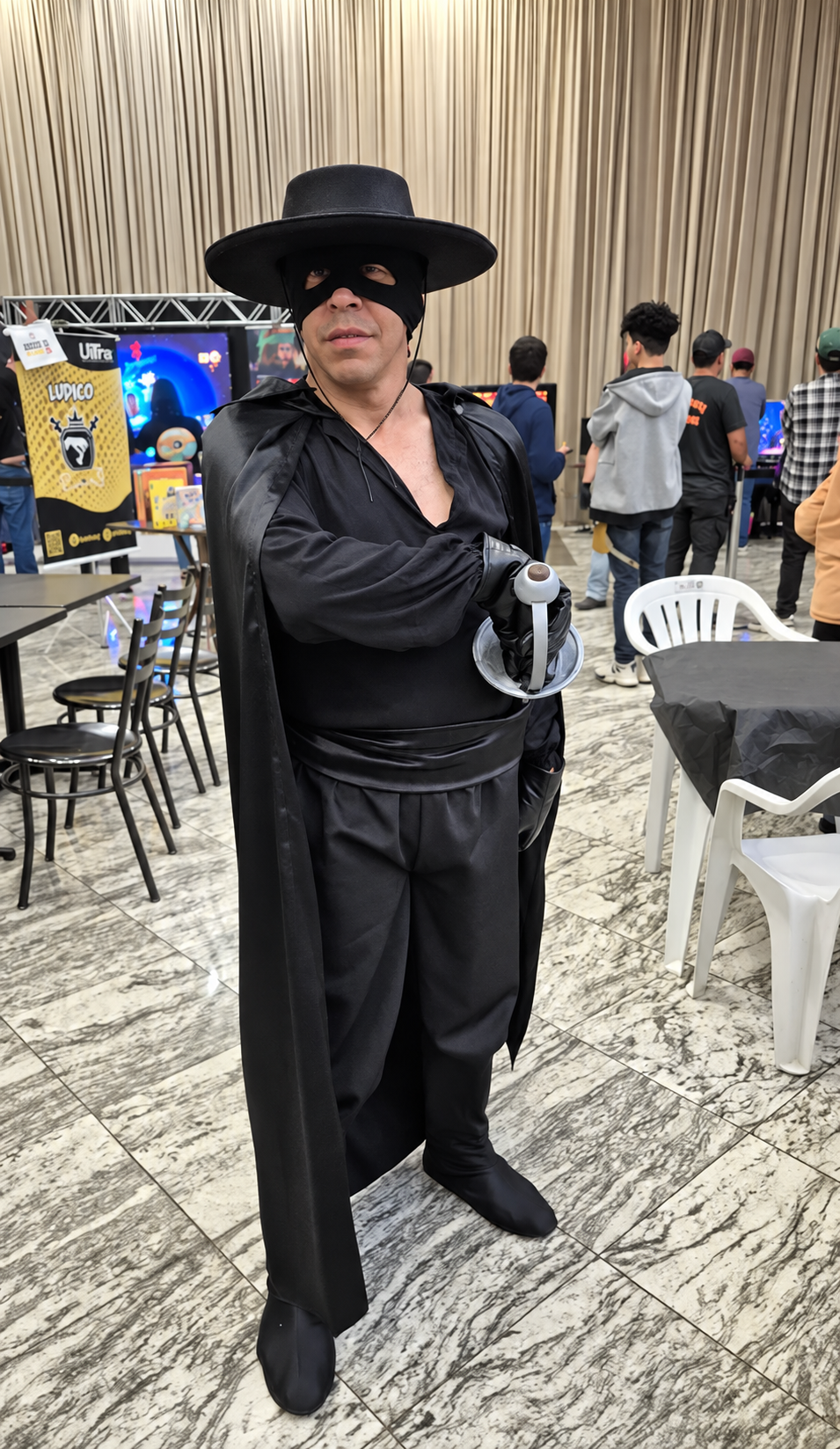 Cosplayer mascarado com capa e chapéu preto